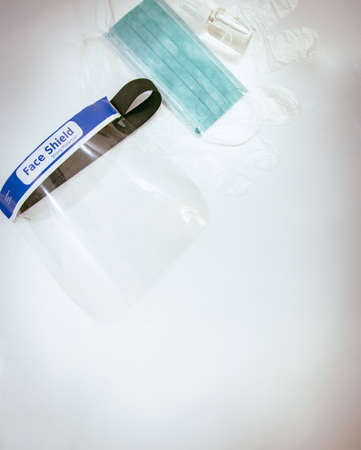 Anti-virus protective kit on white table: mini alcohol spray bootle; blue face mask; face shield and disposable gloves.Vertical image virus free backgroundの写真素材