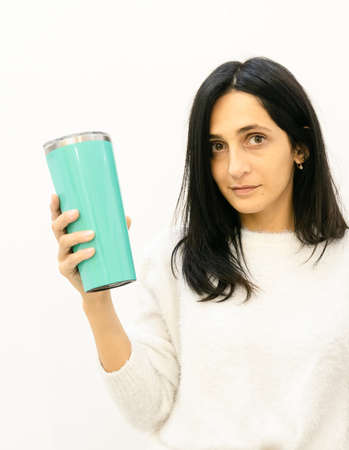 Young caucasian woman holds green flask and looks staright in isolated white wall background