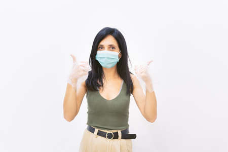 Young attractive brunette woman shows with both hands thumbs up and being positive with three maks on. Recovery and positivity during pandemic.の写真素材