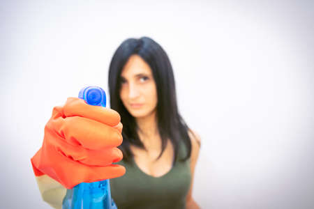 attractive caucasian woman in gloves points straight blue solvent spray bottle isolated in grey...