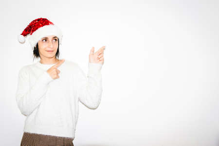 Cute caucausian woman in Christmas outfit points index fingers to the right white blank space. Advert and greetings blank space concept.の写真素材