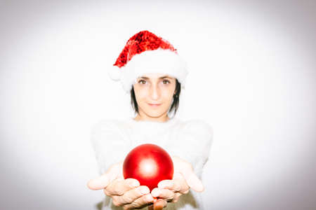Woman in Christmas outfit holds in two hands red xmas decoration shiny ball gift. Happiness and...