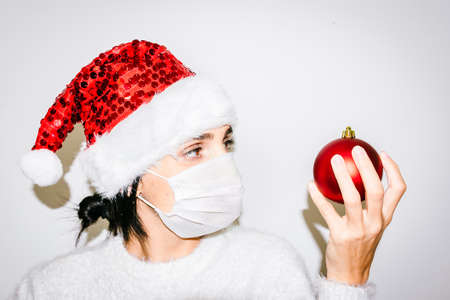 Close up face of caucasian Woman with red bling sparkle xmas hat holding red xmas decoration ball. Hope and Christmas celebrations concept 2020.の写真素材