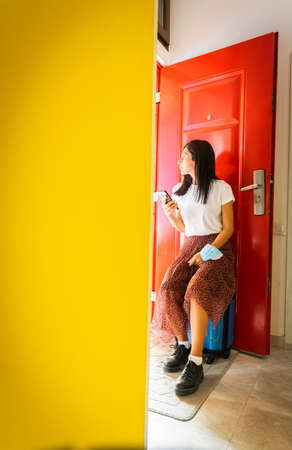 Young caucasian woman sits on the blue suitcase and looks outside holding phone. Concept of waiting...