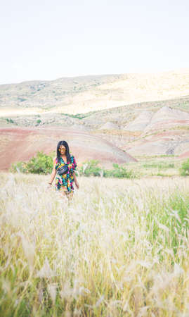 Vertical image of a girl from from distance going throug the wil field with rainbow color mountains in background. Conceptual summer nostalgic memoriesの写真素材