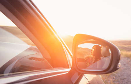 Relaxed girls sitting in a car reflection on side mirror with sun flare and nature in the background  Blank space image.の写真素材