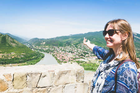 Young female woman in blue dress points finger to Mtskheta town in Georgia.Torusim and travel in caucasus.の写真素材