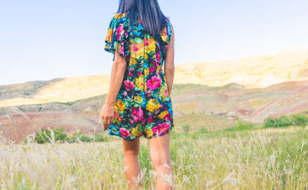 Young attractove girl with short beautiful flower dress walks down the meadow field with colorful mounatins in the abcground.airy summer vive background image.の写真素材