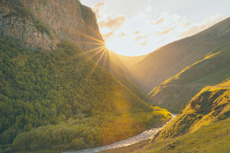 Road and the river surounded by picturesque mountains and setting suns flare. Dramatic landscapes of Georgia.の写真素材