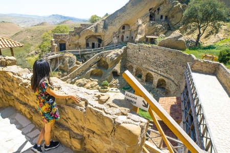 girl tourist stands by the wall and looks down to the yard of David Gareji monastery with cave formations in the backgroundの写真素材