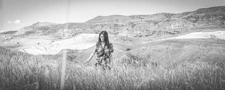 Young girl coming throug the field with mountains in the background. Conceptual summer nostalgic...