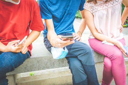 close up of three person in casual colorful clothes sitting and browsing their phones with masks in their hands. Social media and interacting lifestyle during pandemic in 2020の写真素材