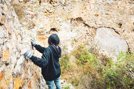 Young woman carefully climgs walks along the wall isolated and surounded by walls in historical site. Exploration and  adventure concept. Georgia. Berdiki pholadauri fortress.の写真素材