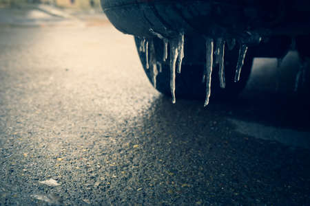 Close up view icicles car bumber with tires on frosty road concept. Slippery road conditions conceptの写真素材
