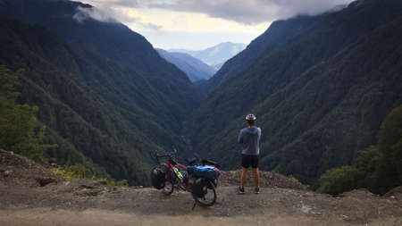 Caucasian male Cyclist enjoying tranquil mountain panorama with touring bicycle standingの写真素材