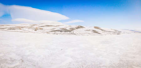 Small Person stands on frozen lake surrounded with mountains