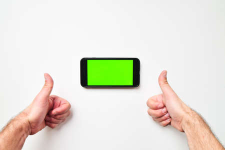 Male big hands and mobile smartphone with green screen in horizontal position background with two hand thumbs up finger. Mock up mobile screen blank spaceの写真素材