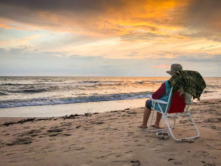 Elderly woman sitting on foldable chair on Palanga beach enjoy watching sunset and sea in calm tranquil evening. Lithaunia summer holiday vacation.の写真素材
