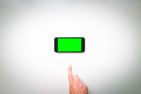 Male person hand finger pointed up smartphone with green screen in panorama position isolated on green background with thumbs up finger. Mock up mobile screen blank spaceの写真素材
