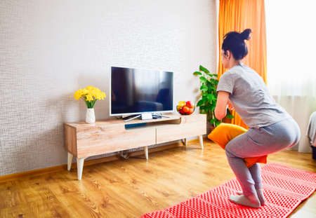 Young beautiful slim athletic caucasian woman in living room on mat exercise follow tutorial on smartphone with yellow pillow tension knees.の写真素材