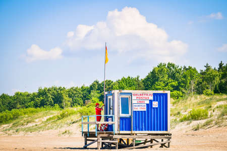 Young woman lifeguard on beach by cabin put yellow flag up. Weather conditions on the beach.のeditorial素材