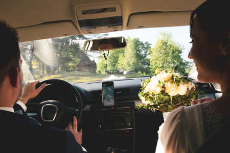 Close up view bride and groom inside car drive to wedding party to meet friends outdoors . Wedding couple celebrates marriage in Lithuaniaの写真素材