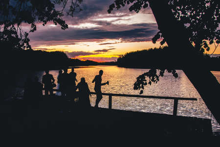 Group of friends silhouette by lake having fun in nature on celebrations. Blank space fun party...