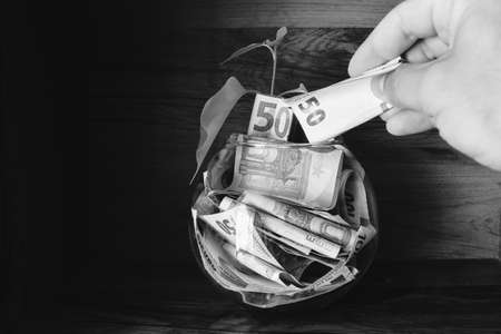 Hand holds fifty euro paper note adds to savings bowl. Investment holdings in high currency.