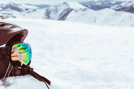 Black helmet with skiing goggles on snow with white snowy mountains landscape backgroundの写真素材