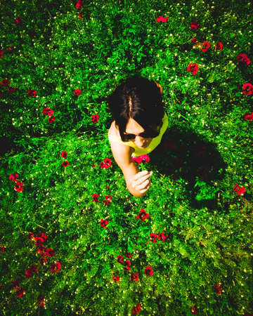 Young Caucasian woman pick poppy flower and smell outdoors. Concept freedom spring being in nature healthy lifestyle.の写真素材