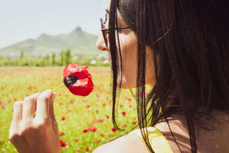 Young Caucasian woman pick poppy flower and smell outdoors. Concept freedom spring being in nature healthy lifestyleの写真素材