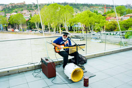 Georgia, Tbilisi - april 30, 2022: STreet musician play live music for tourist on peace bridge in city center with river background. One man band in publicのeditorial素材