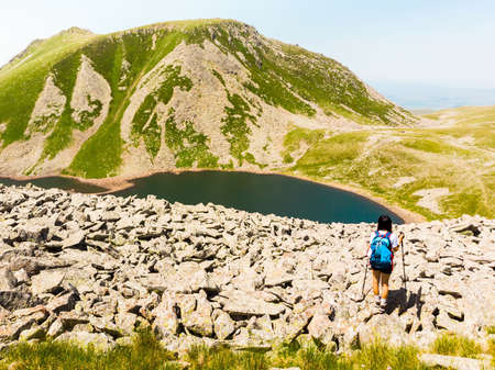 Aerial close up - one Female hiker hike on mountain top in hot summer day. Inspirational young woman with backpack and nordic walk sticks hike in mountains aloneの写真素材