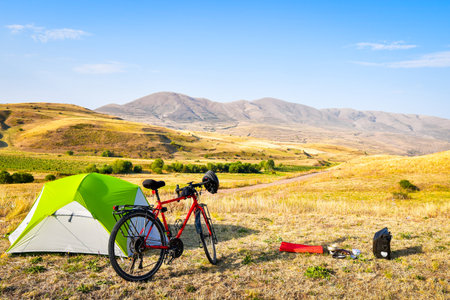 Panorama of unloaded touring red bicycle by green tent. Camping and bicycle touring concept Travel around Armenia by bicycle in mountains in autumnの素材 [FY310191454444]