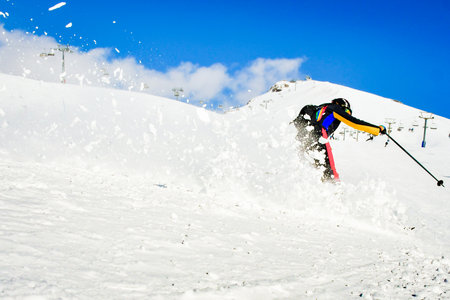 Dynamic picture of a skier on the piste in Alps. Woman skier in the soft snow. Active winter holidays, skiing downhill in sunny day.Ski rides on the track with swirls of fresh snowの写真素材