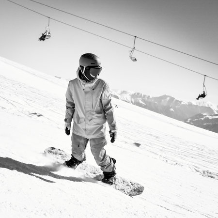 Snowboarder on slope go down fast with mountains background. Black and white sports photographyの写真素材