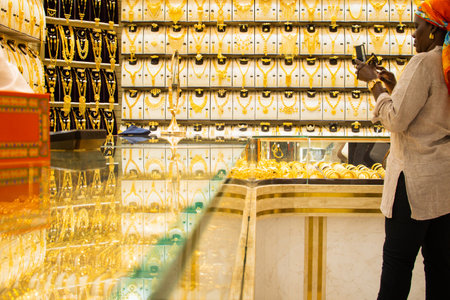 Dubai, UAE - 12th october, 2022 : african woman wear golden luxury accessories take photos with smartphone in old souk store in old Dubaiのeditorial素材
