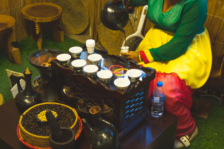 Dubai, UAE - 12th october, 2022: african lady pour traditional coffee to cup from pot. Old coffee preparation methods with vintage technologyのeditorial素材