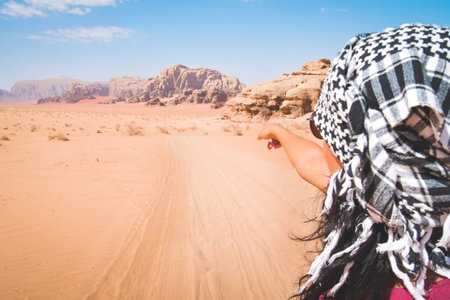 Back view female tourist stand watch point finger to wadi rum desert landscape in jordan desert-famous nature reserve in middle east. Explore Jordan bannerの写真素材