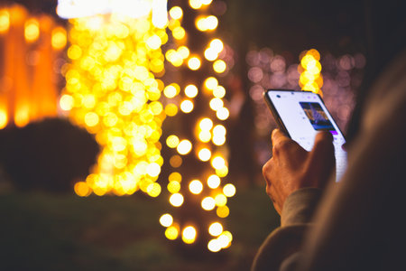Woman hand hold and use phone for messaging outdoors at night, share photos online on xmas holiday celebrationsの写真素材
