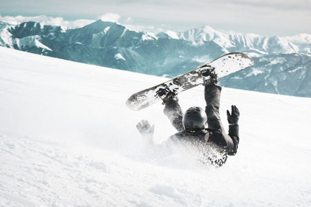 Snowboarder fall down on back with snow splashes on snowy off-piste ski slope and old chair lift at background. Caucasus Mountains in sunny winter day. Black and white toned image.の写真素材