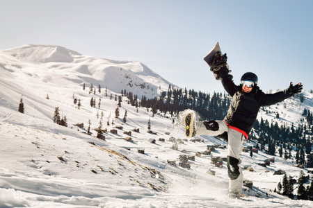 Snowboarder holding his snowboard over head kick snow happy feeling great in ski resort excited on holiday vacation solo. Sunny weather powder dayの写真素材