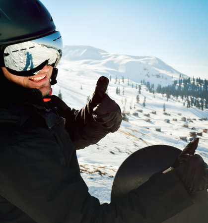 Freerider snowboarder smiling to the camera, showing thumb up, standing to the top of the mountain with his snowboard, copyspace ski-lift people lifestyle winter holidays vacation tourismの写真素材