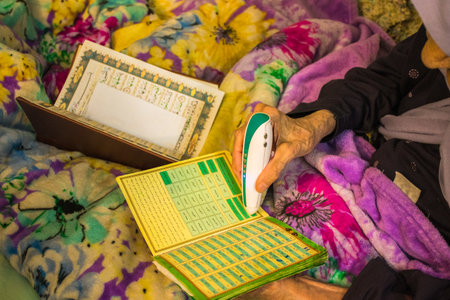 YAzd, Iran - 22nd june, 2022: Elderly woman at home use electric Koran read pen to read in arabicのeditorial素材