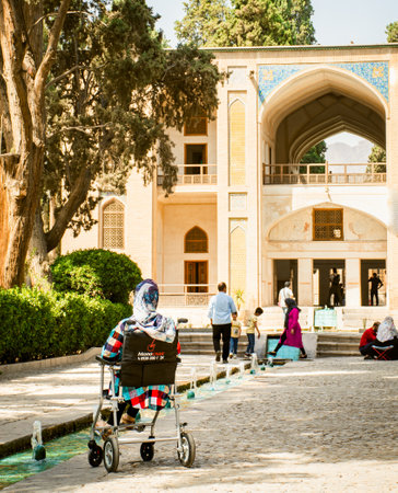 Kashan, Iran - 27th may, 2022: Muslim woman in wheelchair visit travel destination. Family in traditional persian Fin garden Kashan, Iranのeditorial素材