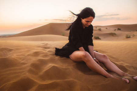 Traveler explorer girl sit in Desert and let sand fall from the hand.Silhouette of woman playing with sand on sunset in summer vacation as twilightの写真素材
