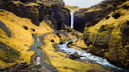 Female tourist walk on pathway visit famous Kvernufoos waterfall landmark. Yellow grass hills on Kvernufoss waterfall. Majestic summer view of pure water river in Iceland, Europeの写真素材