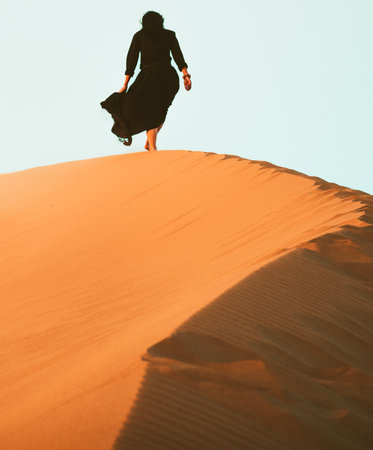 Low angle tracking view beautiful woman in long dress feet follow walk on KAshan desert dunesの写真素材