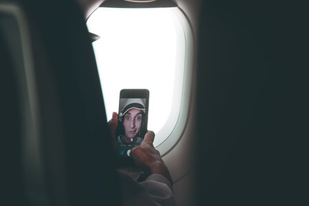 Young caucasian woman passenger pose for selfie touch touch screen smartphone in plane cabin seat before flight. Funny girls on vacation post on social media conceptの写真素材