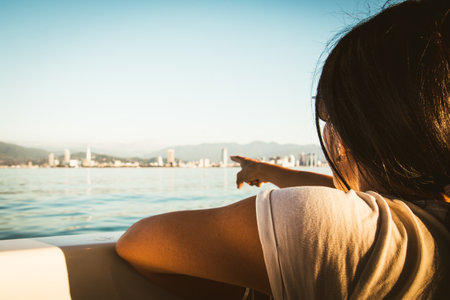 Tourist Woman sits on the boat and looks to scenic view of Batumi and landmarks during romantic sunset.の写真素材